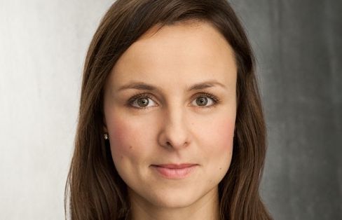 Porträt einer Frau mit langen, braunen Haaren und braunen Augen, vor einem neutralen Hintergrund.