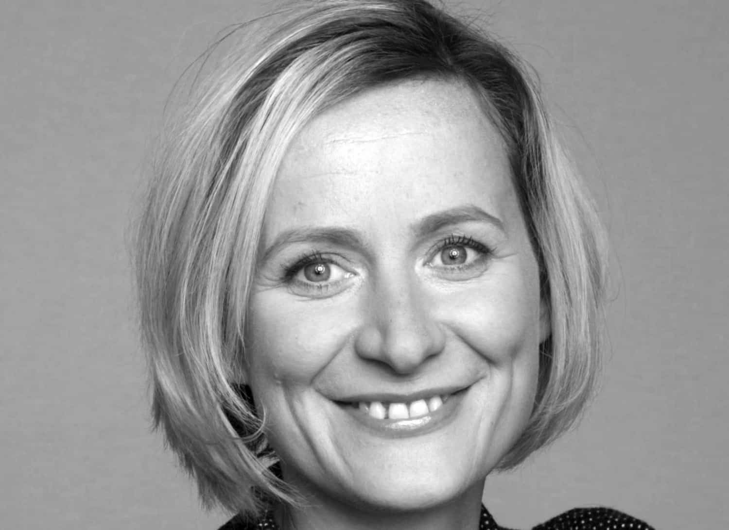 Schwarz-weiß Porträt einer lächelnden Frau mit kurzem, blonden Haar und einem gepunkteten Oberteil.