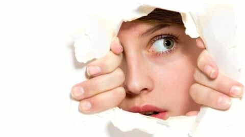 Junge Frau schaut neugierig durch ein Loch in der Wand, ihre Hände halten den Rand des Papiers.