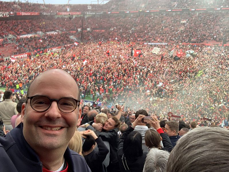 Foto im Selfie-Format von Michael Preuss, dem Kommunikationschef von Bayer, im Fußballstadion.Hinter ihm jubeln und feiern Tausende Fans auf den Rängen und auf dem Rasen. (c) privat