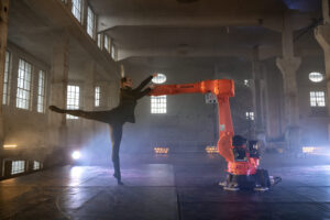 Eine Ballerina tanzt mit einem Greifarm-Roboter. Dazu die Bildunterschrift: Tanz mit einer Ballerina: Kuka nutzt Partnerschaften und Aktionen, um Produkte in Szene zu setzen und so hochwertiges Bildmaterial zu schaffen. © Staatstheater Augsburg/Jan Pieter Fuhr