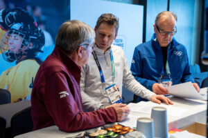 Christian Klaue (m.) leitet seit 2019 die Kommunikation des IOC. Mit Noch-Präsident Thomas Bach (l.) und Sprecher Mark Adams tauscht er sich regelmäßig aus. © IOC