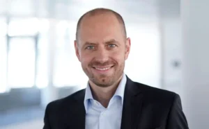 Bruch-Siemens-Energy-1024x636 | KOM - Magazin für Kommunikation Mann mit kurzem Haar und Bart, lächelt in einem modernen Büro. Trägt einen Anzug und ein helles Hemd.