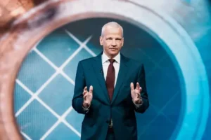 CEO-BASF-2025 | KOM - Magazin für Kommunikation Mann in Anzug steht vor einem großen, runden Bildschirm mit grafischen Mustern und spricht.