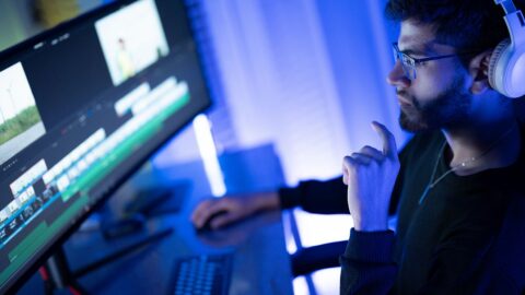 Ein junger Mann mit Kopfhörer schaut auf einen Computerbildschirm, wo ein Videobearbeitungsprogramm läuft. Dazu die Bildunterschrift: Wer Videos erstellen will, braucht keine Videokamera mehr. Aber man sollte wissen, welche KI-Tools nützlich sind. © Getty Images/Suratsak Noikerdmee