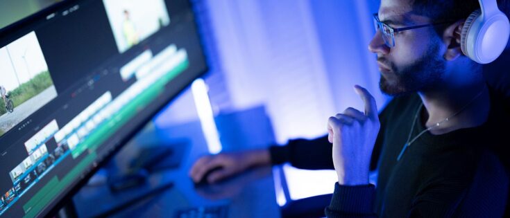 Ein junger Mann mit Kopfhörer schaut auf einen Computerbildschirm, wo ein Videobearbeitungsprogramm läuft. Dazu die Bildunterschrift: Wer Videos erstellen will, braucht keine Videokamera mehr. Aber man sollte wissen, welche KI-Tools nützlich sind. © Getty Images/Suratsak Noikerdmee