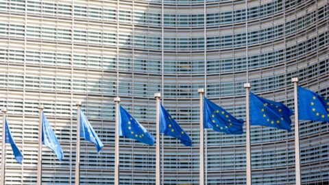 Reihe europäischer Flaggen weht im Wind vor dem Berlaymont-Gebäude der Europäischen Kommission in Brüssel. Dazu die Bildunterschrift: Wesentliche Entscheidungen zur ESG-Regulatorik werden auf EU-Ebene getroffen. © Olivier Rateau / Getty Images