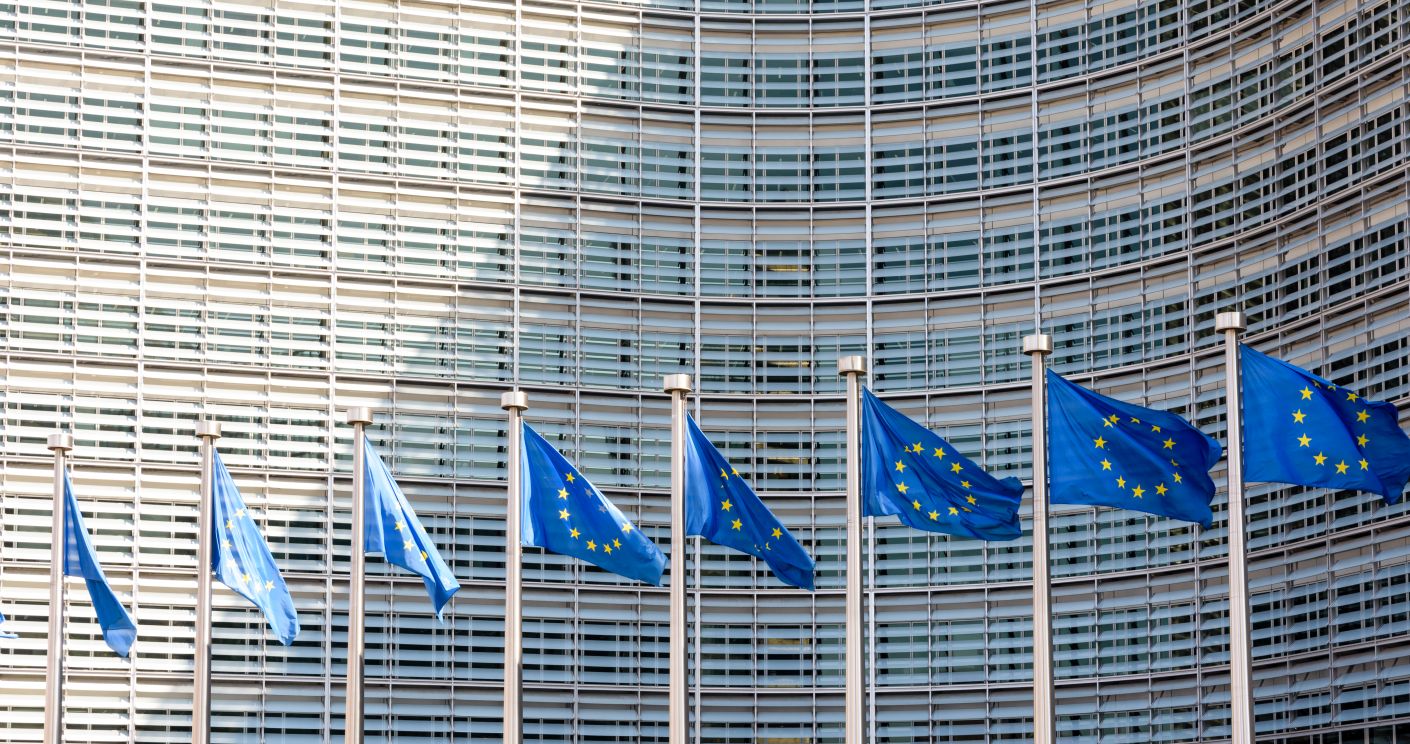 Reihe europäischer Flaggen weht im Wind vor dem Berlaymont-Gebäude der Europäischen Kommission in Brüssel. Dazu die Bildunterschrift: Wesentliche Entscheidungen zur ESG-Regulatorik werden auf EU-Ebene getroffen. © Olivier Rateau / Getty Images
