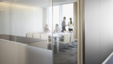 Businessleute in einem Konferenzraum bei einem Meeting, sichtbar durch eine Glaswand. Dazu die Bildunterschrift: Stimmt die Kommunikation nicht, sinkt die Zufriedenheit im Job. © Getty Images/Martin Barraud