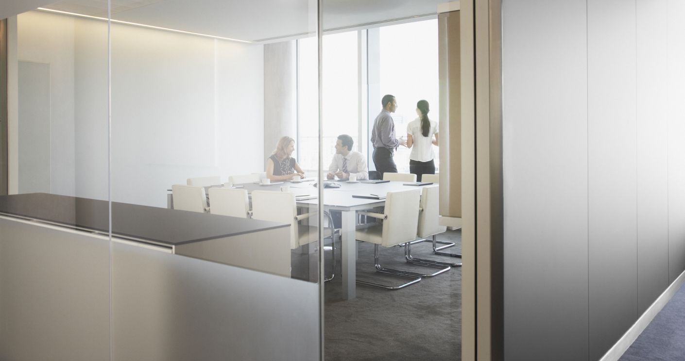 Businessleute in einem Konferenzraum bei einem Meeting, sichtbar durch eine Glaswand. Dazu die Bildunterschrift: Stimmt die Kommunikation nicht, sinkt die Zufriedenheit im Job. © Getty Images/Martin Barraud