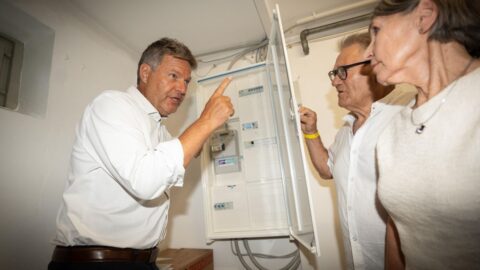 Bundesminister Robert Habeck spricht mit zwei Personen vor einem Stromzähler im Einfamilienhaus über erneuerbare Energien.