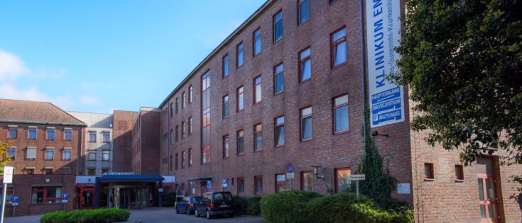 Klinikum Emden: Mehrstöckiges Backsteingebäude mit Eingangsbereich, Bäumen und parkenden Autos.