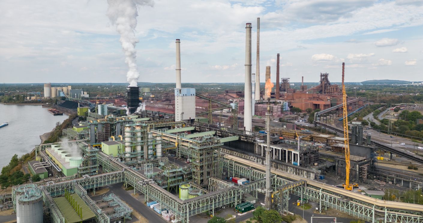 Luftaufnahme des Kokereibetriebs Schwelgern in Duisburg mit rauchenden Schornsteinen und angrenzenden Industrieanlagen.