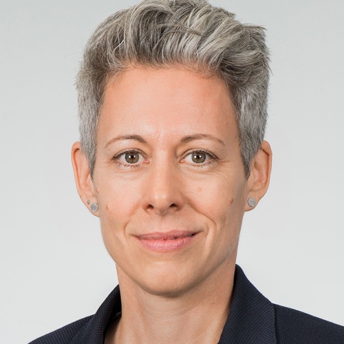 Porträt von Julia Borggräfe mit grauen Haaren, neutralem Hintergrund, in formeller Kleidung, mit einem freundlichen Gesichtsausdruck.