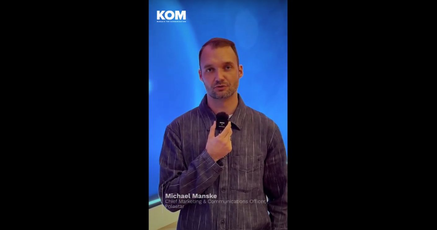 Mann mit Mikrofon und gestreiftem Hemd steht vor einem blauem Hintergrund und spricht in die Kamera.