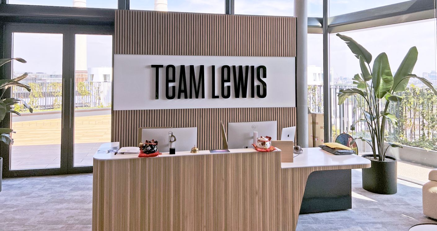 Moderne Empfangstheke mit "TEAM LEWIS"-Schild, Pflanzen im Hintergrund und großen Fenstern mit Aussicht.