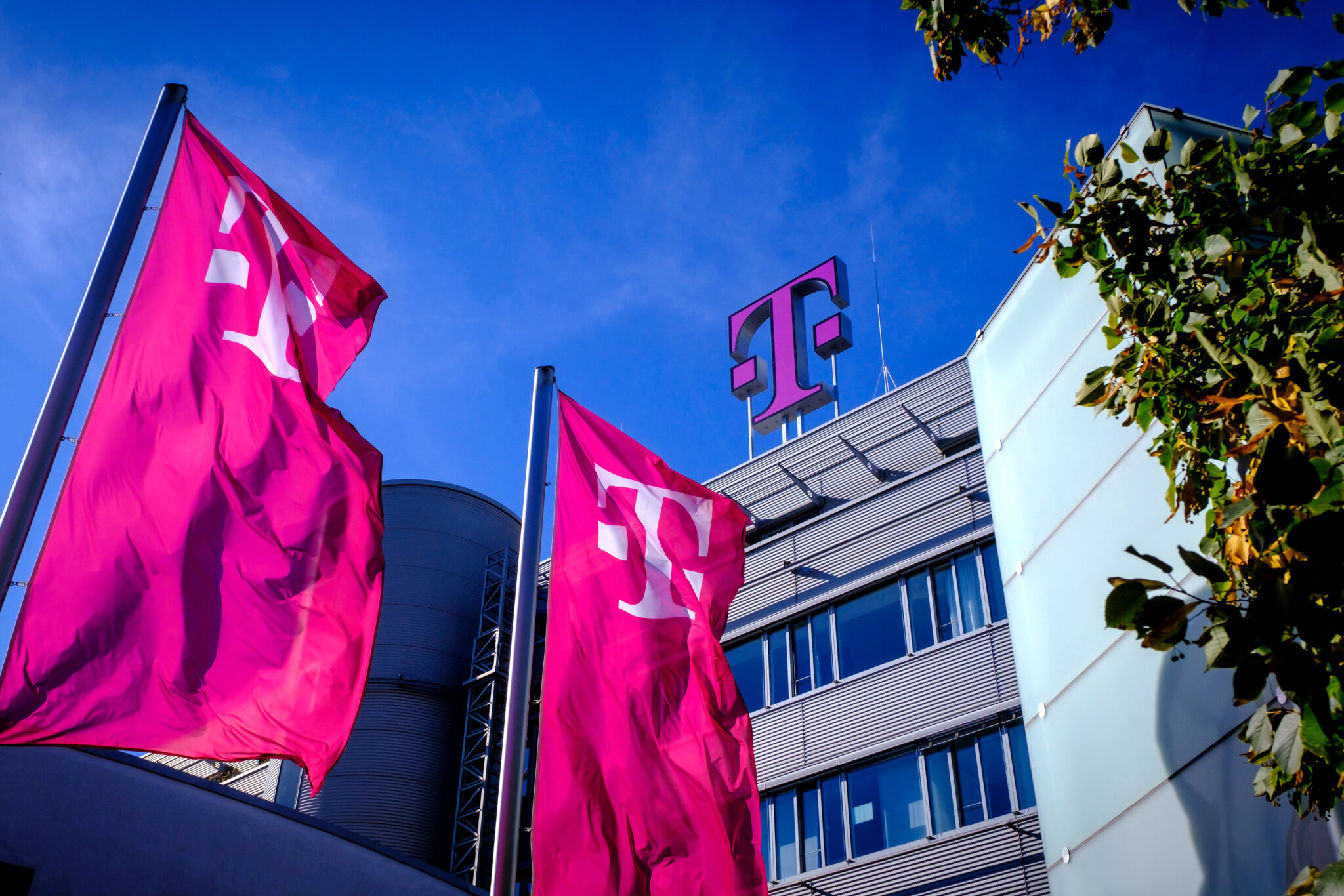 Zwei pinke Telekom-Fahnen wehen vor einem modernen Gebäude mit dem Telekom-Logo auf dem Dach.