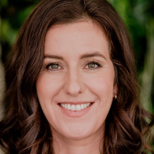 Porträt einer lächelnden Frau mit lockigem, braunem Haar vor einem grünen Hintergrund.