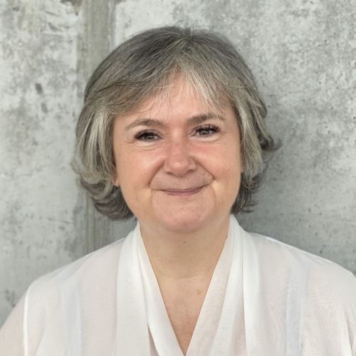 Das Foto zeigt einen Halbkörper-Ausschnitt von Gabriele Horcher in einer weißen Bluse, stehend vor einer Betonwand.