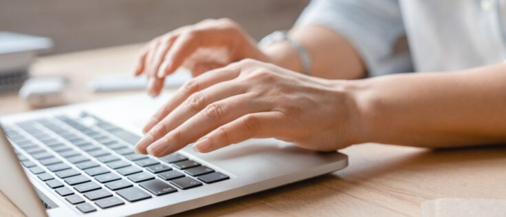 Weibliche Hände tippen auf der Tastatur eines Laptops.