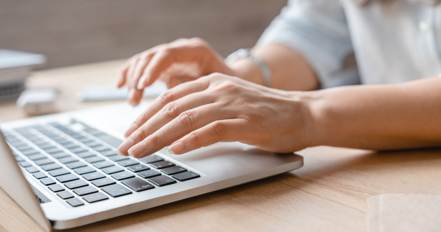 Weibliche Hände tippen auf der Tastatur eines Laptops.