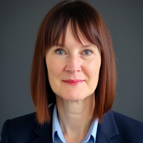 Porträt einer Frau mit schulterlangen, braunen Haaren, in einem blauen Blazer, vor einem grauen Hintergrund.