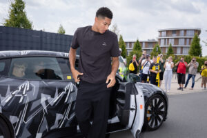 Ein Mann in schwarzem T-Shirt steigt aus einem Auto, während eine Menschenmenge zuschaut.