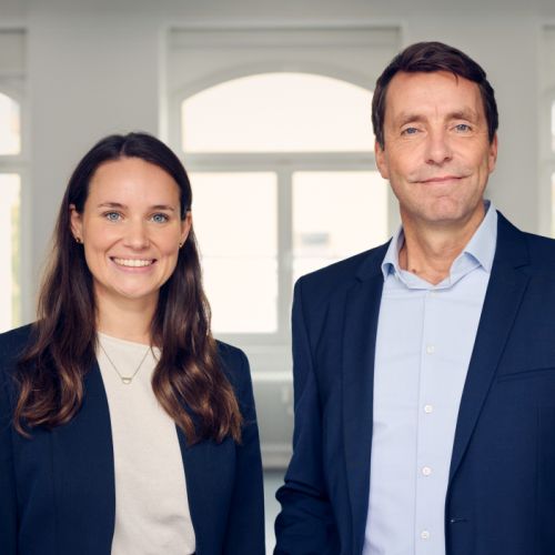 Georg Lahme und Jana Brockhaus stehen lächelnd in einem hellen Raum, beide in formeller Kleidung.