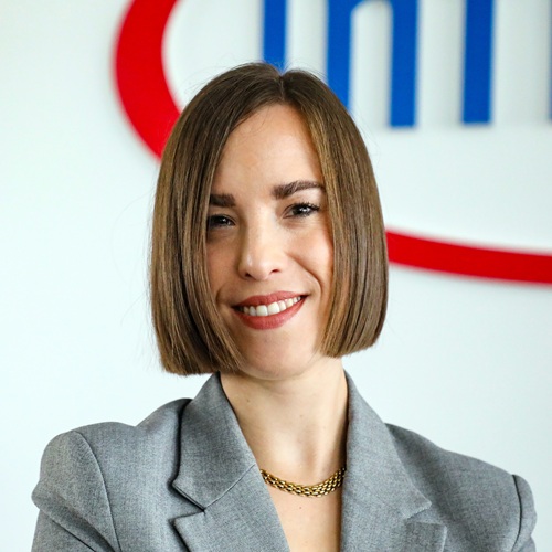 Porträt einer Frau mit schulterlangen, glatten Haaren, die in einem grauen Blazer lächelt, vor einem Infineon-Logo.