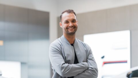 Lächelnder Mann mit verschränkten Armen in einem modernen Ausstellungsraum für Autos.