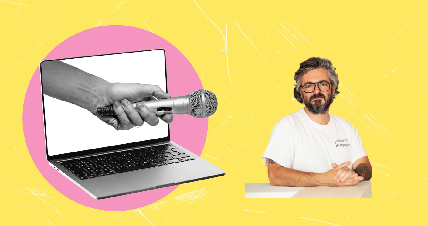 Mann mit Brille sitzt am Tisch, neben einem Laptop mit Mikrofon und pinkem Hintergrund.