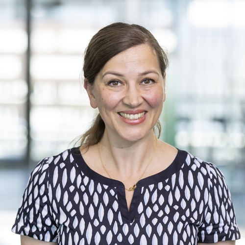 Porträt, lächelnd, mit einem gestreiften Oberteil, vor einem modernen, hellen Hintergrund.