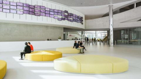 Innenansicht des Merck Innovation Centers mit Sitzgelegenheiten und Personen, die sich in einem großen und modernen Foyer aufhalten.