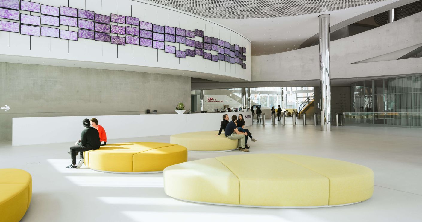 Innenansicht des Merck Innovation Centers mit Sitzgelegenheiten und Personen, die sich in einem großen und modernen Foyer aufhalten.