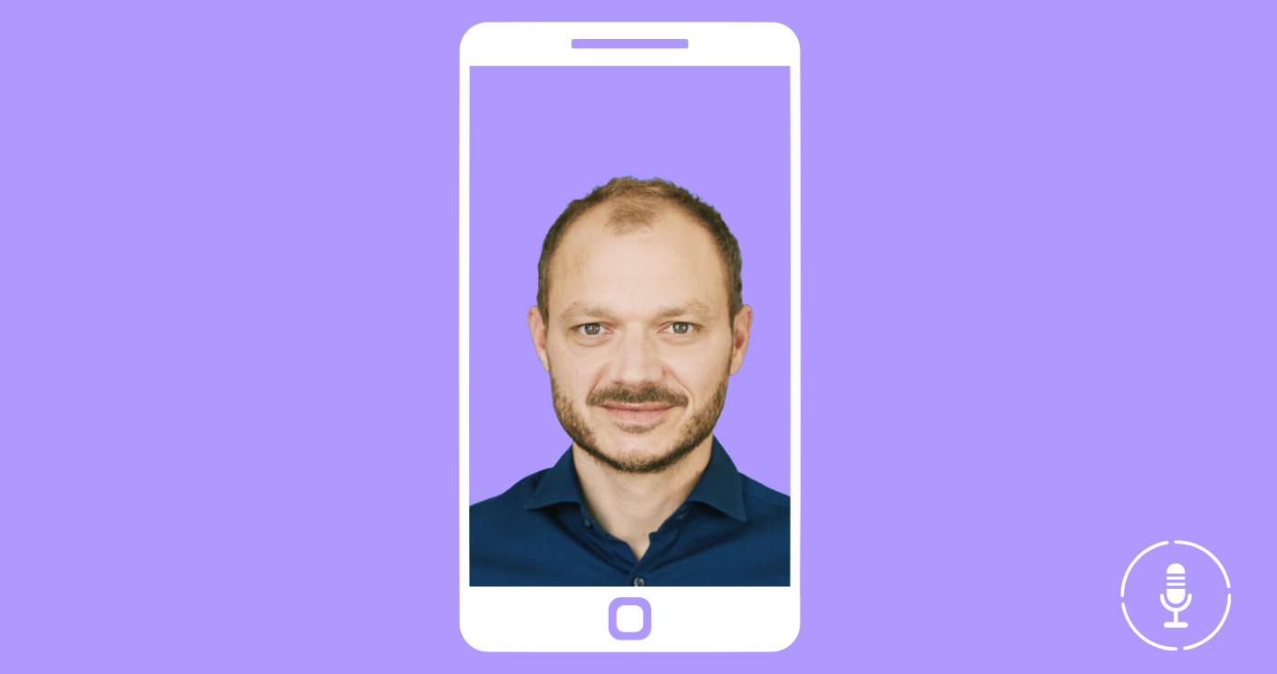 Mann mit kurzem Haar und Bart, in einem blauen Hemd, im Interview auf einem Smartphone-Display vor lila Hintergrund.