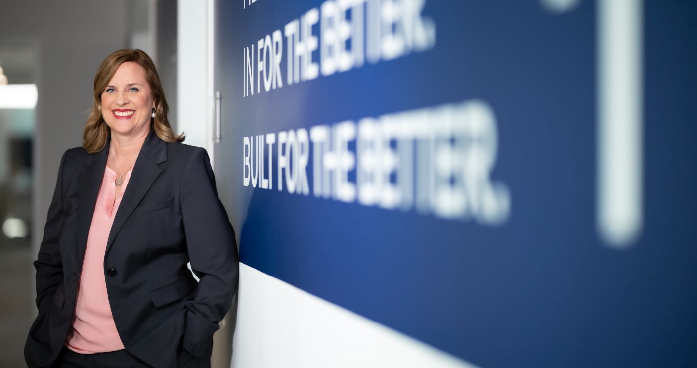 Jill Meiburg in Business-Outfit steht vor einem Board mit dem Unternehmenszweck der GEA Group.