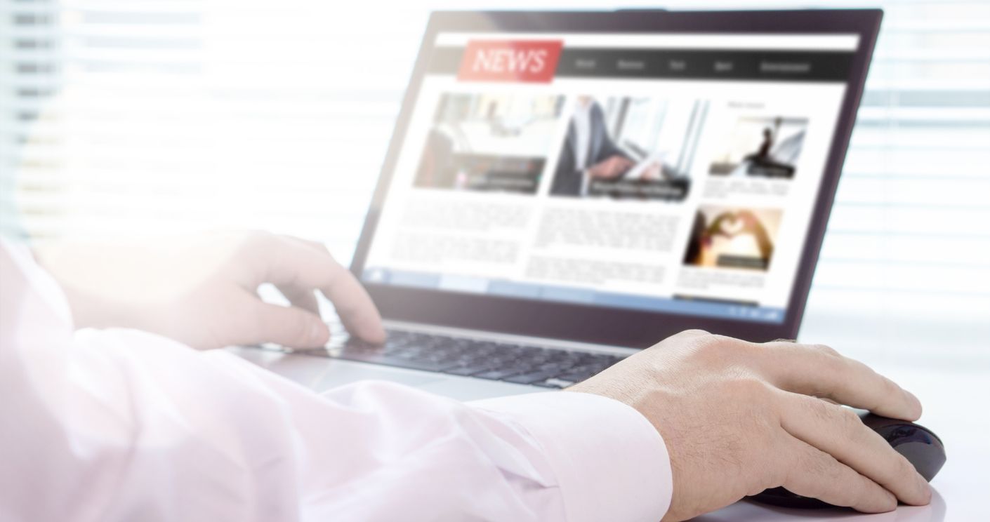 Person mit Laptop, auf dem eine Online-Nachrichtenseite angezeigt wird, während sie mit der Maus interagiert.