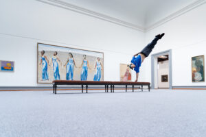 Breakdancer in einem Kunstmuseum, während er einen Handstand auf einer Bank macht, umgeben von Gemälden.