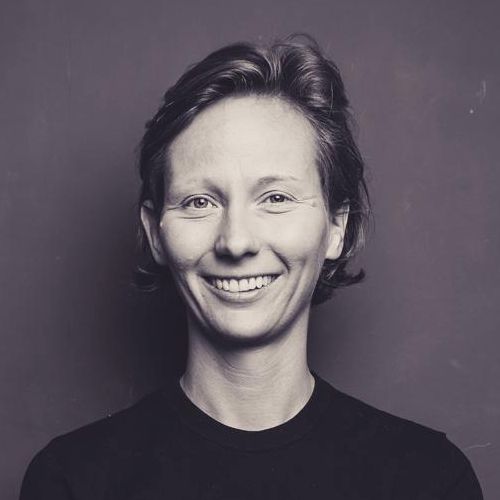 Porträt einer lächelnden Frau mit kurzen Haaren, vor einem neutralen Hintergrund.