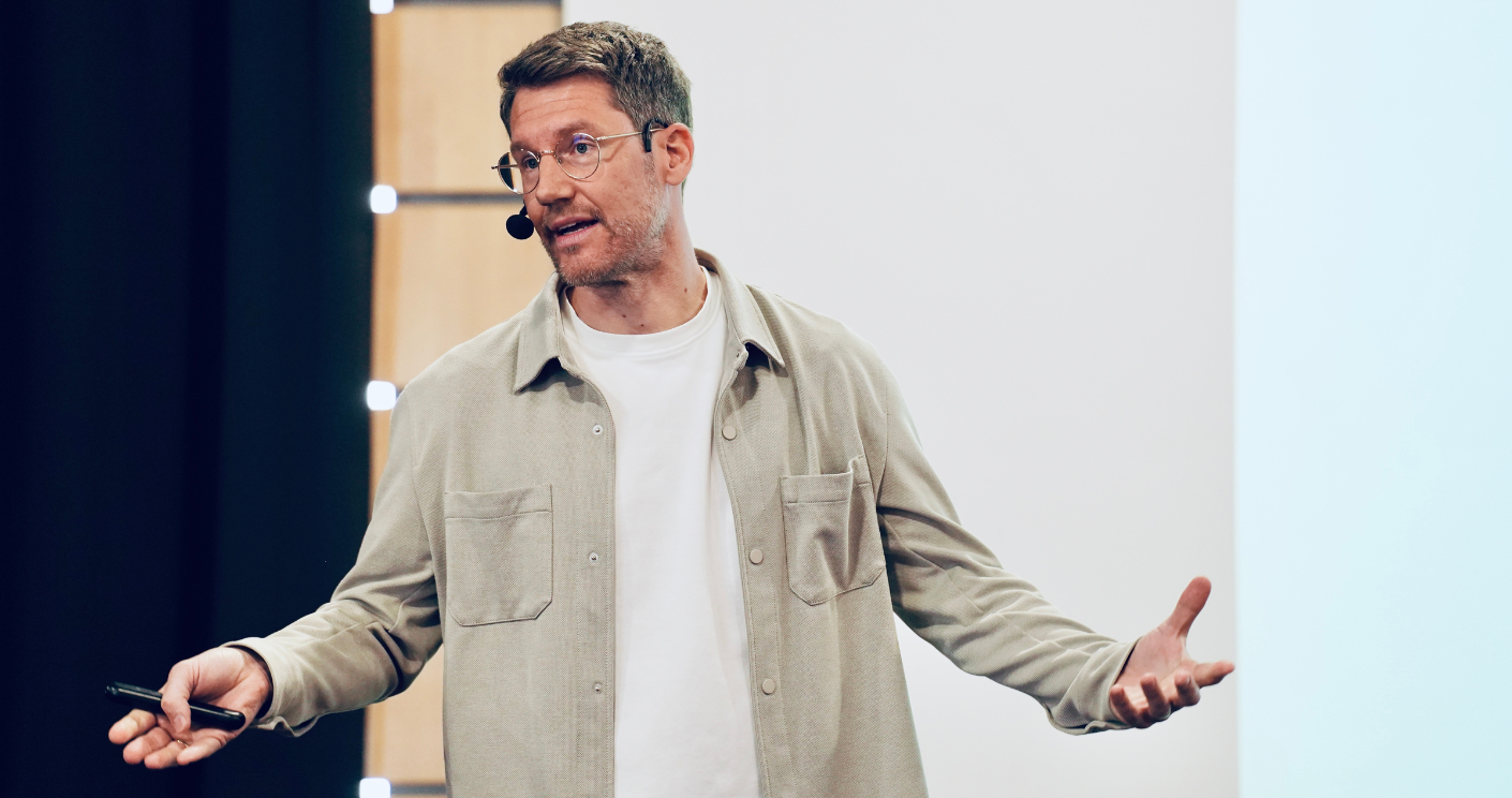 Mann mit Brille und Mikrofon hält Vortrag, gestikuliert mit beiden Händen vor einer Leinwand.