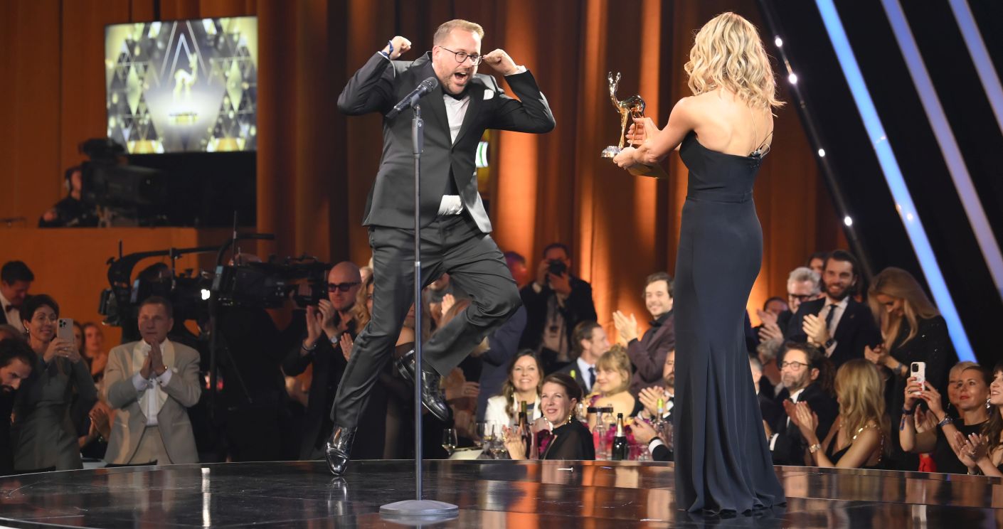 Paul Ronzheimer jubelt auf der Bühne, während Michelle Hunziker ihm einen BAMBI-Preis überreicht. Publikum applaudiert.