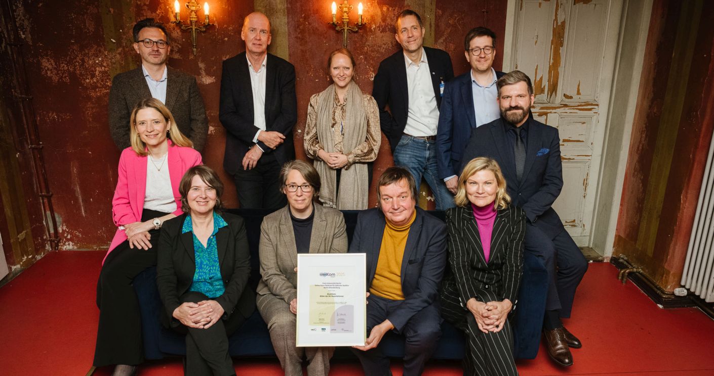Gruppenfoto von zwölf Personen, die auf einem Sofa sitzen und stehen, mit einer Auszeichnung in der Mitte.