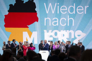 Friedrich Merz und CDU-Mitglieder stehen auf einer Bühne, im Hintergrund ein großes Banner mit dem Motto „Wieder nach vorne"