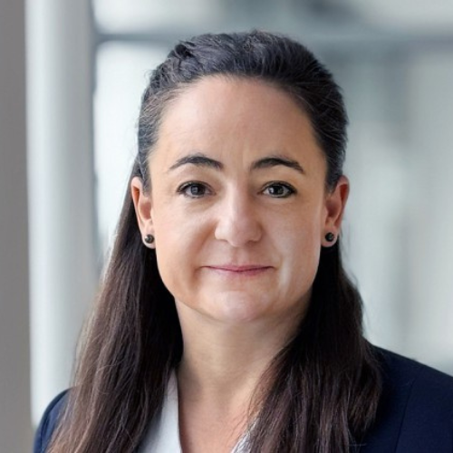 Porträt von Johanna Koch mit langen, dunklen Haaren, in einem blauen Blazer, vor einem hellen, unscharfen Hintergrund.