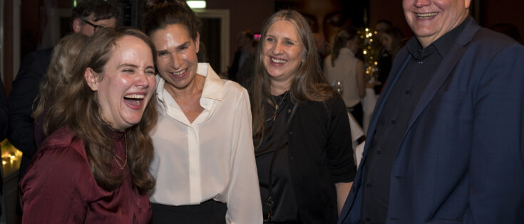 Vier Personen lachen und unterhalten sich in einem festlichen Raum mit gedämpftem Licht.