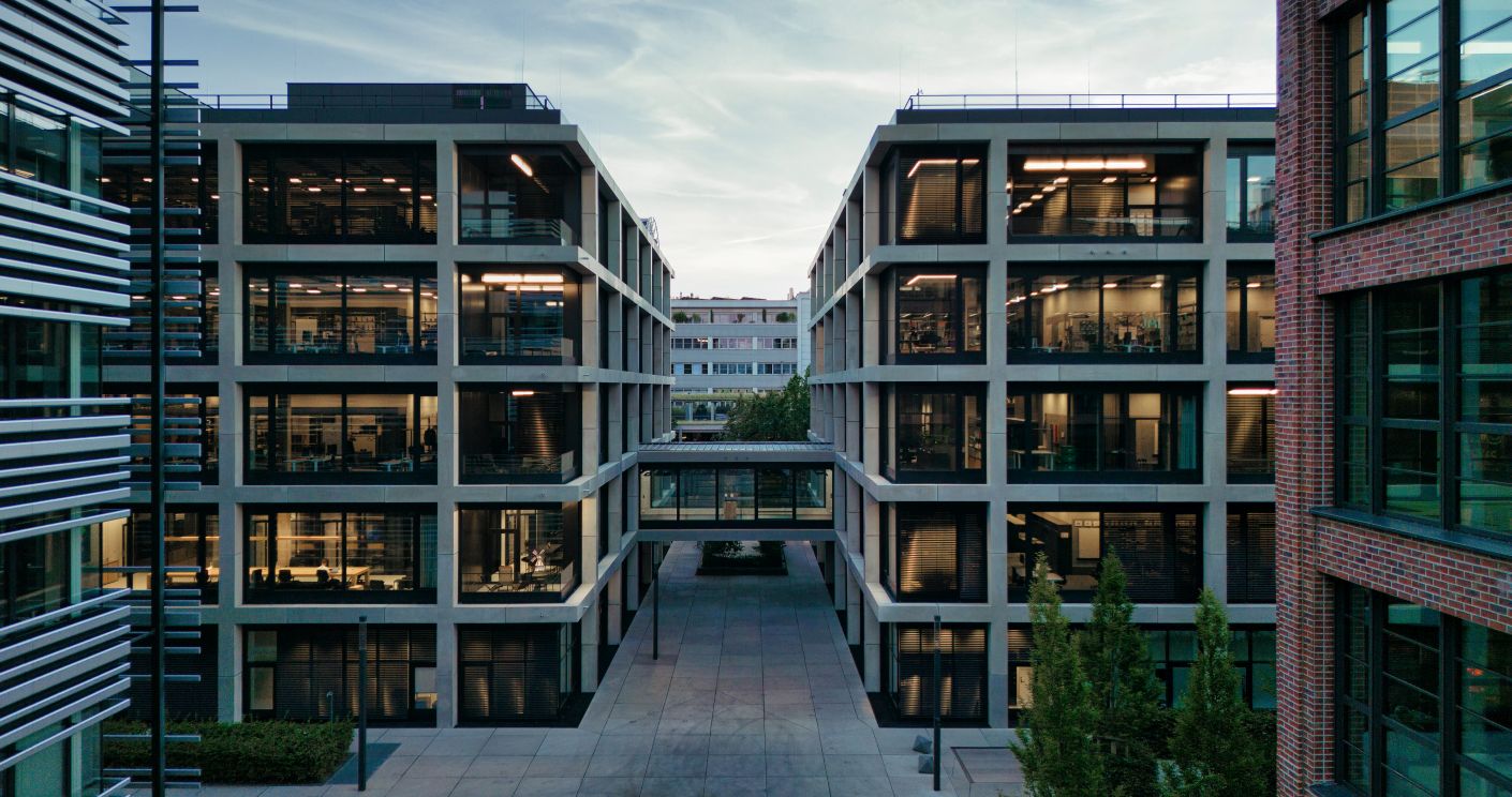 Moderne Bürogebäude mit Glasfassaden und einem zentralen Innenhof, umgeben von Bäumen und städtischer Umgebung.