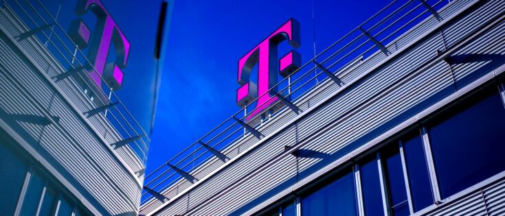 Moderne Gebäudeansicht mit dem pinken Telekom-Logo auf dem Dach und reflektierenden Fenstern unter blauem Himmel.