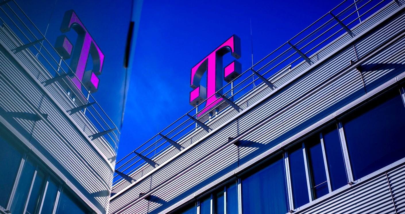 Moderne Gebäudeansicht mit dem pinken Telekom-Logo auf dem Dach und reflektierenden Fenstern unter blauem Himmel.