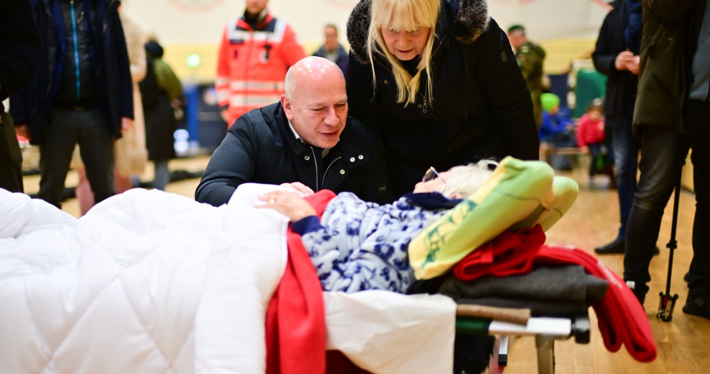 Kai Wegner und Iris Spranger sprechen mit der 97-jährigen Ingeborg in einer Notunterkunft während eines Stromausfalls.