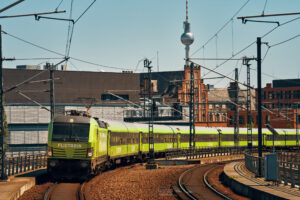 Ein grüner Flixtrain fährt auf Gleisen in Berlin, der Fernsehturm ist im Hintergrund sichtbar.